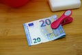 A clothes peg with a banknote, next to laundry soap and red basin, on a wooden plank. Housework bonus concept Royalty Free Stock Photo
