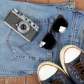 Clothes, shoes and accessories - Top view retro camera, sunglasses, gumshoes and blue jeans on wooden background