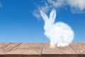 Cloud Easter rabbit on a wooden table against blue sky background.