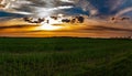 Clouds in the orange rays of the sunset over a green farm field Royalty Free Stock Photo