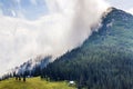 Clouds over top of a mountain with green forest and grass meadow Royalty Free Stock Photo