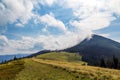 Clouds over top of a mountain with green forest and grass meadow Royalty Free Stock Photo