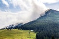 Clouds over top of a mountain with green forest and grass meadow Royalty Free Stock Photo