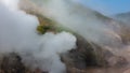 Clouds of steam from an erupting geyser envelop the hillsides.