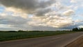 clouds at sunset over an asphalted empty highway that runs between rural fields Royalty Free Stock Photo