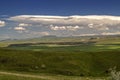 A blue sky with occasional turbulent clouds and Cumulus clouds is approaching the villages and valley of the Geghama mountains in