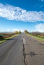 Cloudy country repaired highway/road in bad condition and blue cloudy sky. Green and yellow/orange fields, sunny landscape Royalty Free Stock Photo