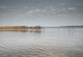 Cloudy gray blue sky and calm water of lake with autumn grass in it. Peaceful landscape with matural monochrome scene