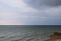 A cloudy grey sky shrouds the white foamy tipped teal waters of this beach