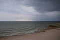 A cloudy grey sky shrouds the white foamy tipped teal waters of this beach