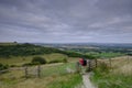 Cloudy overcast summer sunrise over the South Downs Way footpath from A middle aged male walker with backpack admiring the view