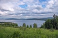 Cloudy sammer landscape of the lake with a blooming hill and mountains in the distance.