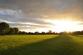 Cloudy sky, sun rays, green field, trees and beautiful sunset in Ireland