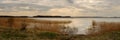 cloudy spring day. wide panoramic view from the grassy coast to a large calm lake with coastal reeds and the opposite shore under