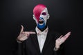 Clown and Halloween theme: Scary clown with pink hair in a black jacket with candy in hand on a dark background in the studio Royalty Free Stock Photo