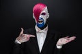 Clown and Halloween theme: Scary clown with pink hair in a black jacket with candy in hand on a dark background in the studio Royalty Free Stock Photo