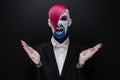 Clown and Halloween theme: Scary clown with pink hair in a black jacket with candy in hand on a dark background in the studio Royalty Free Stock Photo