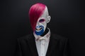 Clown and Halloween theme: Scary clown with pink hair in a black jacket with candy in hand on a dark background in the studio Royalty Free Stock Photo