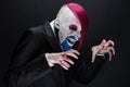 Clown and Halloween theme: Scary clown with pink hair in a black jacket with candy in hand on a dark background in the studio Royalty Free Stock Photo