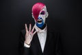 Clown and Halloween theme: Scary clown with pink hair in a black jacket with candy in hand on a dark background in the studio Royalty Free Stock Photo