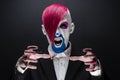 Clown and Halloween theme: Scary clown with pink hair in a black jacket with candy in hand on a dark background in the studio Royalty Free Stock Photo