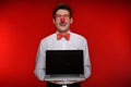 Clown with laptop. Cheerful man with clown holding a laptop while standing isolated on red