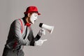 The clown, MIM, is holding a Megaphone. Expression of emotions. On a gray background