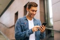 Clsoe-up portrait of happy handsome young man using mobile phone standing on stairs of modern office building. Royalty Free Stock Photo