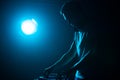 Club DJ plays music in bright blue stage lights. Disc jockey mixing musical tracks with sound mixer on concert