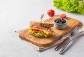 Club sandwich on a plate of bacon, cheese, tomato and lettuce on a wooden board with olives