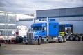 Cluster of big rigs semi trucks tractors and semi trailers standing on the warehouse parking lot in industrial park area