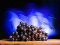 Cluster of dark grapes on wooden board and dark background with colorful blue light painting. Fresh fruit product. Tasty desert.