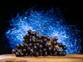 Cluster of dark grapes on wooden board and dark background with colorful blue light painting. Fresh fruit product. Tasty desert.