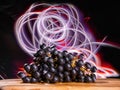 Cluster of dark grapes on wooden board and dark background with colorful light painting. Fresh fruit product. Tasty desert. Still