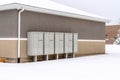 Cluster metal mailboxes with pedestals against wall of building with snowy roof