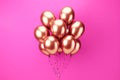 A cluster of pink and gold balloons floating in front of a pink backdrop