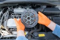 Auto mechanic wearing protective work gloves holds used clutch disc friction plate over a car engine Royalty Free Stock Photo