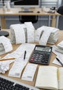 A cluttered office desk features a large calculator displaying \
