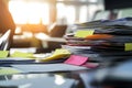 a cluttered desk with a huge stack of paperwork and colorful sticky notes, illuminated by bright sunlight streaming through a near Royalty Free Stock Photo