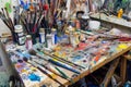 A cluttered work desk with scattered paint brushes and tubes of paint AI generated Royalty Free Stock Photo