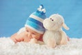 Cmile baby in hat, hugging toy on a white bedspread, on a blue b Royalty Free Stock Photo
