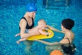 Coach training newborn child floating at swimming courses mom and baby. Women focusing on little child on swimming board