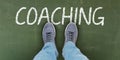 A person stands on a chalkboard with the word `COACHING`