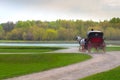 Coachman in cloak sits in coach with horse and hold reins in spring park Royalty Free Stock Photo