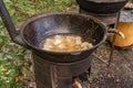 Coarsely chopped potatoes are fried in boiling oil in a cast-iron cauldron on a wood-burning stove.