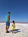 The coast of the salty Pink Lake in the Crimea. A man in blue breeches and a little boy in yellow clothes with a bottle of water. Royalty Free Stock Photo