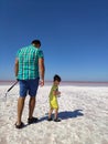 The coast of the salty Pink Lake in the Crimea. A man in blue breeches and a little boy in yellow clothes with a bottle of water Royalty Free Stock Photo