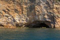 Kayakers passing a sea cave set into a sheer cliff