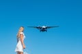 Coastal Encounter: Girl in White Dress on Stones, Plane in Blue Skies