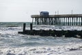 Coastal landscape showing the sandy beach, rough ocean and a pier and wooden jetty extending into the ocean